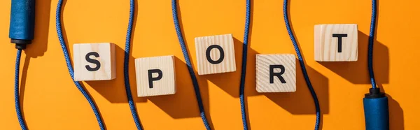 Panoramic shot of jumping rope near wooden cubes with sport lettering on yellow — Stock Photo