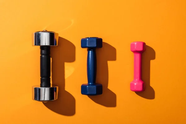 Top view of black, blue and pink metallic dumbbells on yellow — Stock Photo
