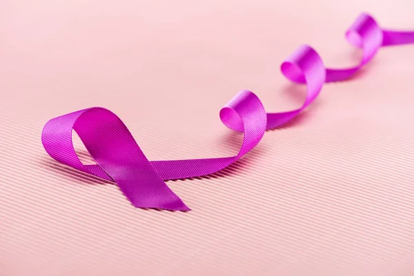 Purple ribbon on pink textured surface — Stock Photo