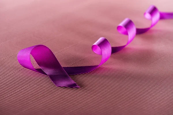 Purple ribbon on pink texture background in shadow, violence concept — Stock Photo