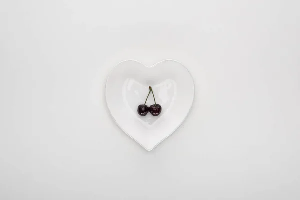 Vue de dessus des cerises rouges et fraîches sur plaque blanche en forme de coeur — Photo de stock