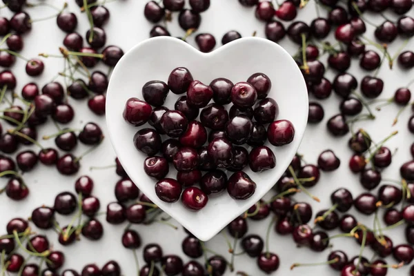 Vista superior de cerezas maduras, frescas, enteras y dulces en plato blanco - foto de stock