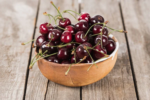 Ciliegie rosse, fresche, intere e mature sulla ciotola sul tavolo di legno — Foto stock