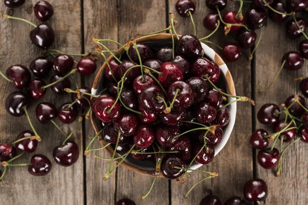 Top view of red, fresh, whole and ripe cherries covered with droplets on bowl on wooden surface — Stock Photo