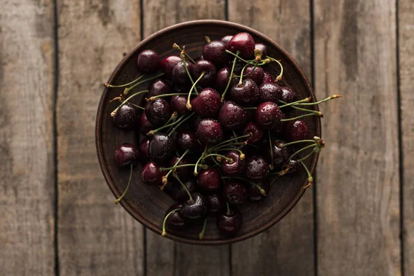 Top view of red, fresh, whole and ripe cherries covered with droplets on plate on wooden surface — Stock Photo