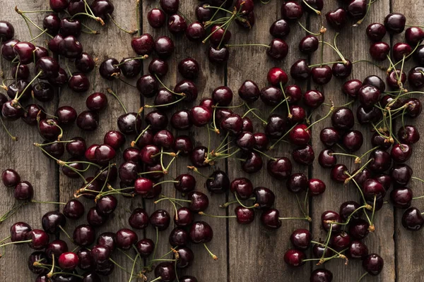 Vista superior de cerezas rojas, frescas, enteras y maduras en la superficie de madera - foto de stock