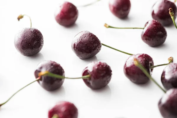 Enfoque selectivo de cerezas frescas, enteras y maduras cubiertas con gotas de agua sobre fondo blanco - foto de stock