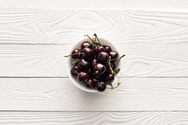 Vista superior de cerezas frescas, dulces y maduras en un tazón sobre fondo de madera - foto de stock