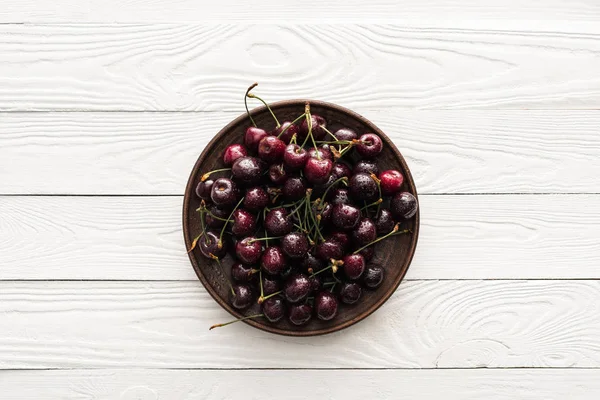 Vista superior de cerezas frescas, dulces y húmedas en plato sobre fondo de madera - foto de stock