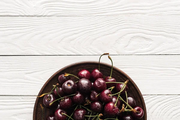 Vista superior de cerezas frescas, dulces y lavadas en plato sobre fondo de madera - foto de stock