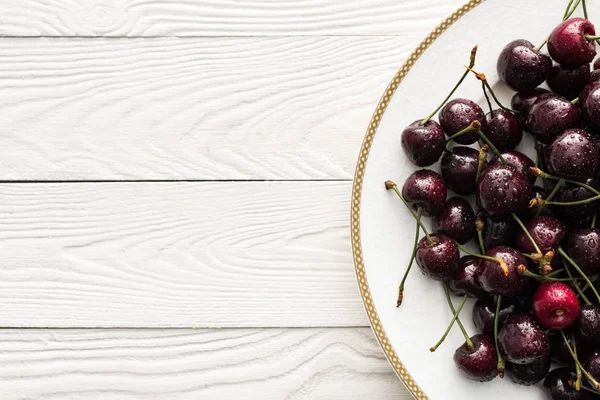 Vue de dessus des cerises fraîches, sucrées et mûres recouvertes de gouttelettes sur plaque blanche — Photo de stock