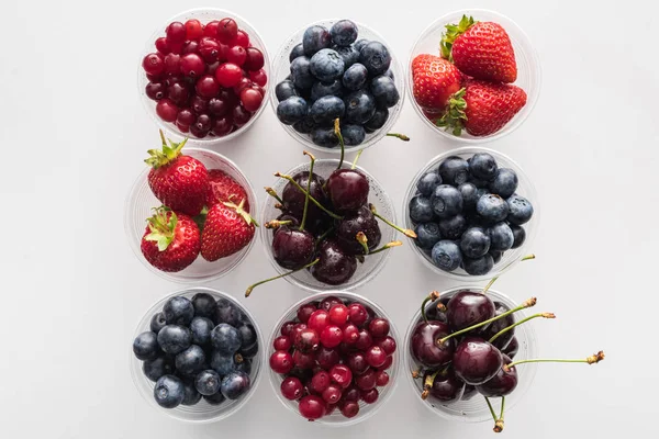 Vista superior de arándanos, fresas, arándanos y cerezas enteros en tazas de plástico - foto de stock