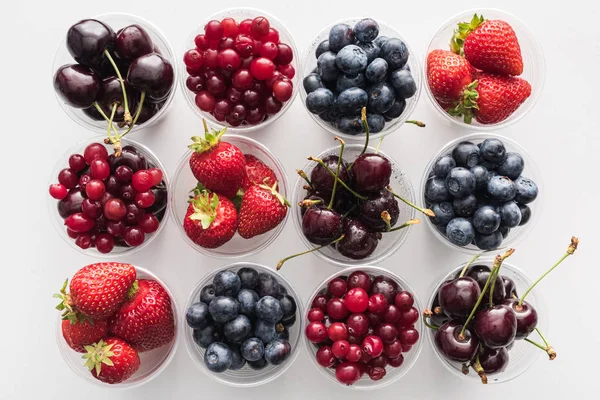 Vista dall'alto di mirtilli rossi interi, fragole, mirtilli e ciliegie in bicchieri di plastica — Foto stock