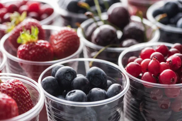 Selective focus of cranberries, strawberries, blueberries and cherries in plastic cups — Stock Photo