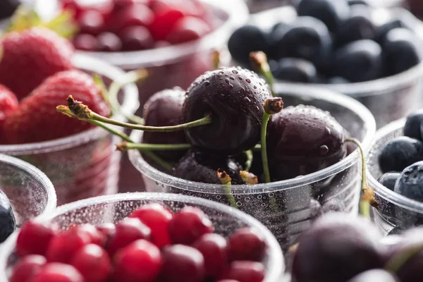 Selective focus of cranberries, strawberries, blueberries and washed cherries in plastic cups — Stock Photo