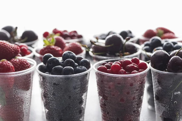 Selective focus of cranberries, strawberries, blueberries and wet cherries in plastic cups — Stock Photo