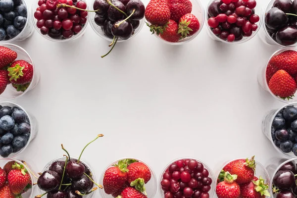 Draufsicht auf ganze Preiselbeeren, Erdbeeren, Blaubeeren und Kirschen in Plastikbechern auf weißem Hintergrund — Stockfoto