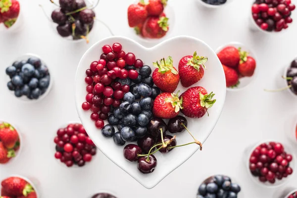 Top view of whole cranberries, strawberries, blueberries and cherries on heart shaped plate — Stock Photo
