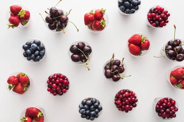 Vista dall'alto di mirtilli rossi interi, fragole fresche, mirtilli e ciliegie in bicchieri di plastica — Foto stock