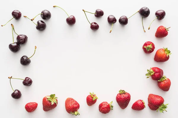 Vista dall'alto di ciliegie dolci e fresche ricoperte da gocce d'acqua e fragole rosse su sfondo bianco — Foto stock