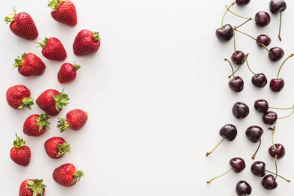 Vista superior de cerezas dulces y frescas y fresas rojas sobre fondo blanco - foto de stock