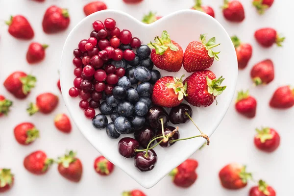Vista superior de arándanos dulces, arándanos, fresas y cerezas en forma de corazón plato - foto de stock