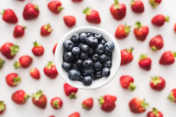 Vue du dessus des bleuets doux sur le bol et des fraises sur le fond — Photo de stock