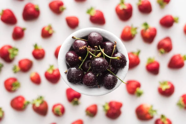 Vista dall'alto di ciliegie dolci su ciotola e fragole su sfondo — Foto stock