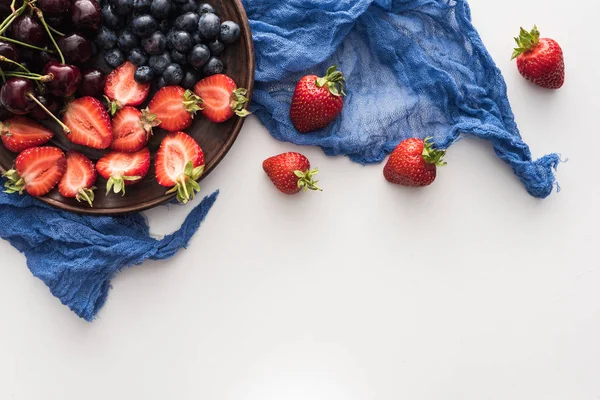 Vue de dessus des myrtilles douces, cerises et fraises coupées sur assiette avec chiffon bleu — Photo de stock