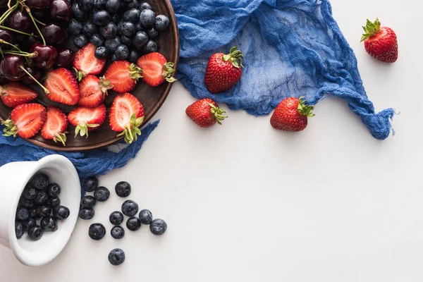 Top view of sweet blueberries on bowl, cherries and cut strawberries on plate with blue cloth — Stock Photo
