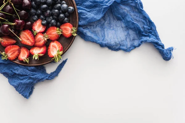 Vista superior de arándanos dulces, cerezas y fresas cortadas en plato con paño azul - foto de stock