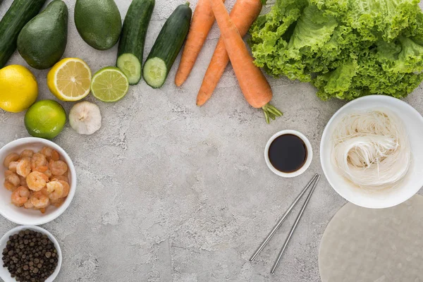 Top view of lemons, limes, avocados, carrots, black pepper, shrimps, soy sauce, rice paper, garlic,noodles and lettuce on table — Stock Photo