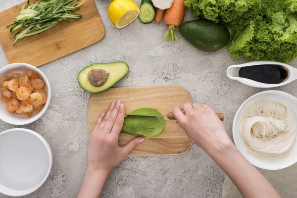 Vista superior de la mujer cortando aguacate con cuchillo en la tabla de cortar - foto de stock