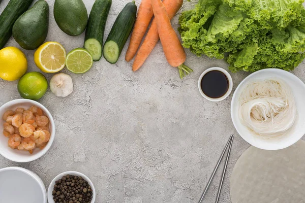 Vista superior de limones, limas, aguacates, zanahorias, pimienta negra, camarones, salsa de soja, papel de arroz, ajo, fideos y lechuga en la mesa - foto de stock