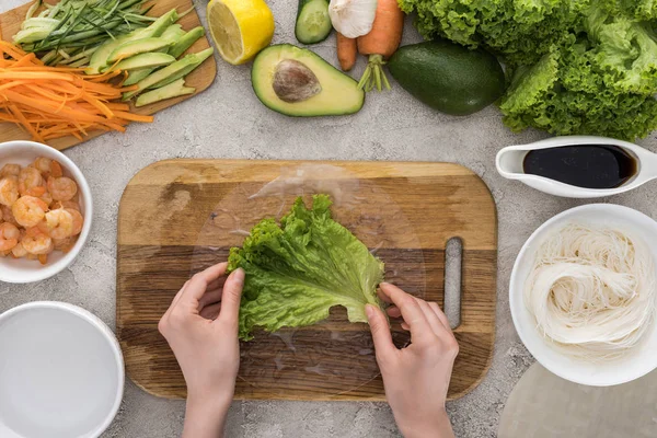 Top view of woman putting lettuce on rice paper, on cutting board — Stock Photo