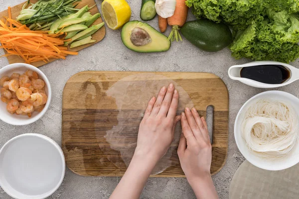 Vista superior de la mujer sosteniendo papel de arroz en la tabla de cortar - foto de stock