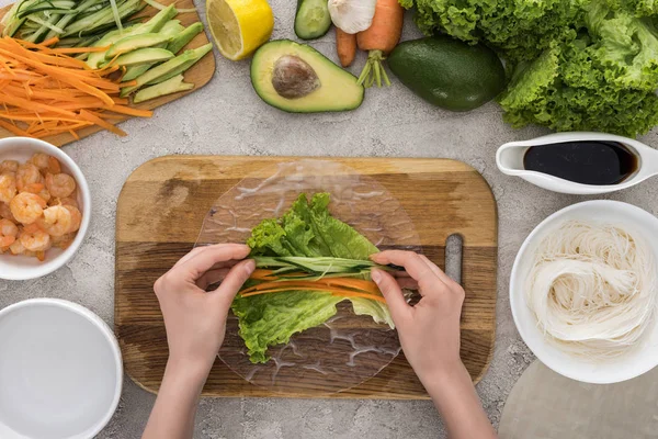 Ansicht von oben: Frau legt geschnittene Avocado und Karotte auf Salat, auf Schneidebrett — Stockfoto