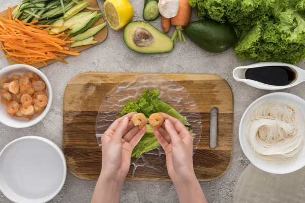 Vista superior de la mujer poniendo camarones en la lechuga, en la tabla de cortar - foto de stock