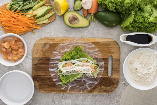 Top view of shrimps, lettuce and noodles on rice paper, on cutting board — Stock Photo