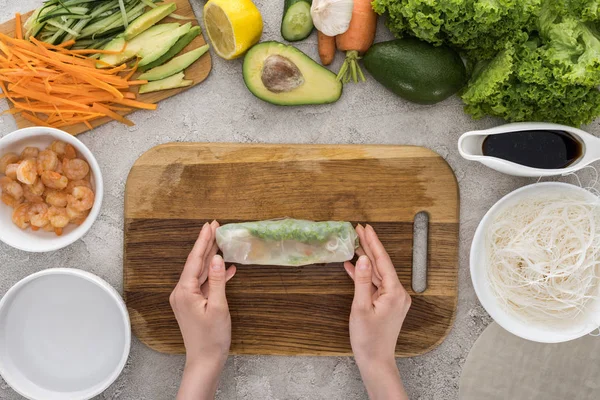 Vista superior de la mujer haciendo rollo en la tabla de cortar entre los ingredientes - foto de stock