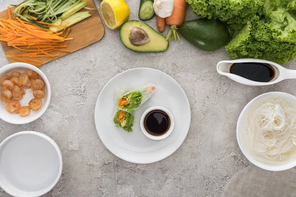 Vista superior de sabrosos rollos de primavera con salsa de soja en plato blanco - foto de stock