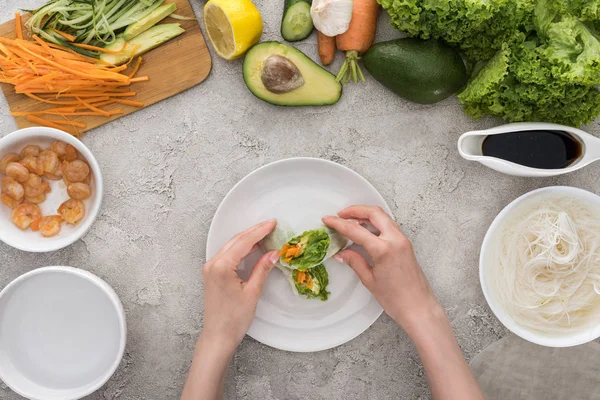 Vista superior de la mujer que sirve sabrosos rollos de primavera en plato blanco - foto de stock