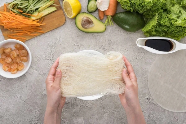 Vista superior de la mujer sosteniendo fideos entre las materias primas - foto de stock