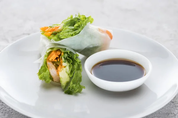 Sabrosos y servidos rollos de primavera con salsa de soja en plato blanco - foto de stock