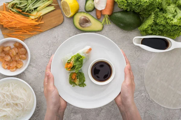 Top view of woman holding plate with tasty spring rolls and soy sauce — Stock Photo