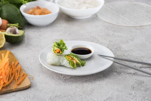 Rouleaux de printemps savoureux et servis avec sauce soja sur plaque blanche avec bâtons métalliques — Photo de stock