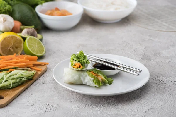 Sabrosos y servidos rollos de primavera con salsa de soja en plato blanco con palos de metal - foto de stock