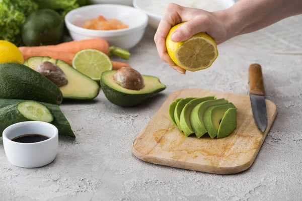 Vista recortada de la mujer exprimiendo limón en aguacate cortado en la tabla de cortar - foto de stock