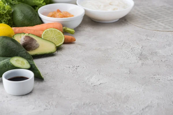 Limão, abacates, cenouras, camarões, molho de soja, papel de arroz, macarrão e alface na mesa — Fotografia de Stock