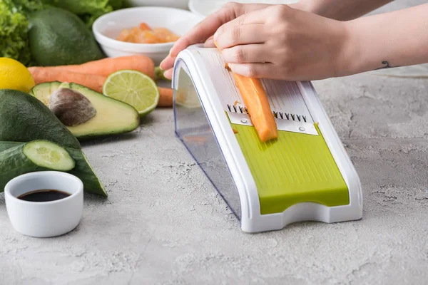 Cropped view of woman grating carrot among ingredients — Stock Photo